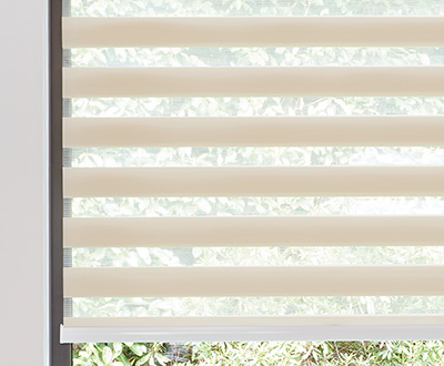 Double Roller Shades for windows made of Windansea in Canyon cover a small window looking out to a green expanse